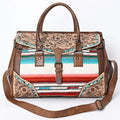 Handwoven western leather duffel trunk with floral tooling, colorful striped textile, and adjustable shoulder strap.