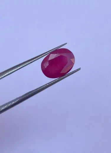 Oval faceted red gemstone held by metal tweezers