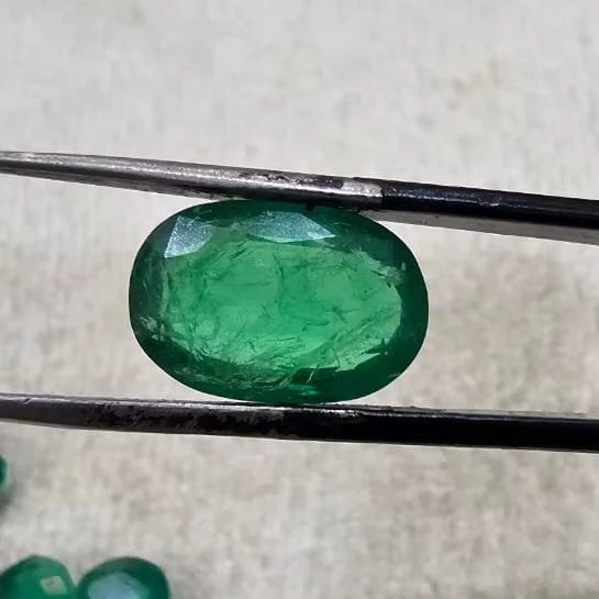 Large green oval gemstone in tweezers, close-up on felt