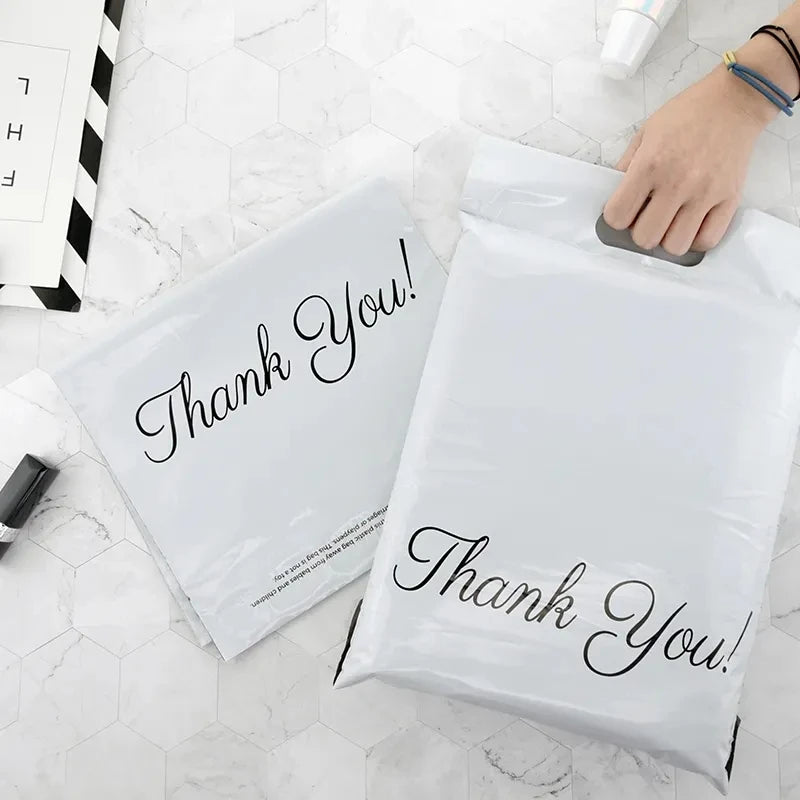 Two white plastic poly mailer bags with black "Thank You!" print, flat lay