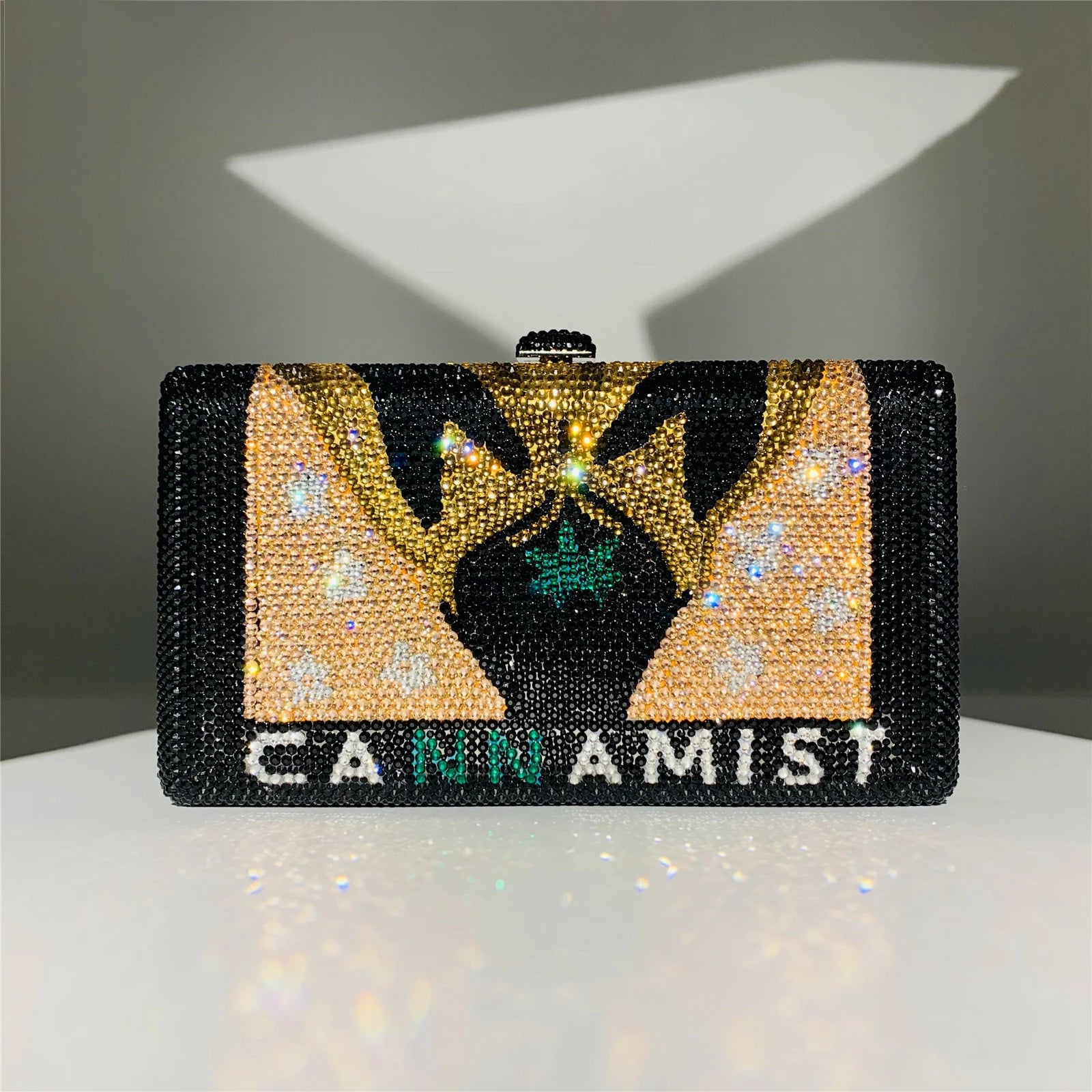 Luxury crystal clutch bag with "CANNAMIST" text, black and gold rhinestone design for formal evening wear.