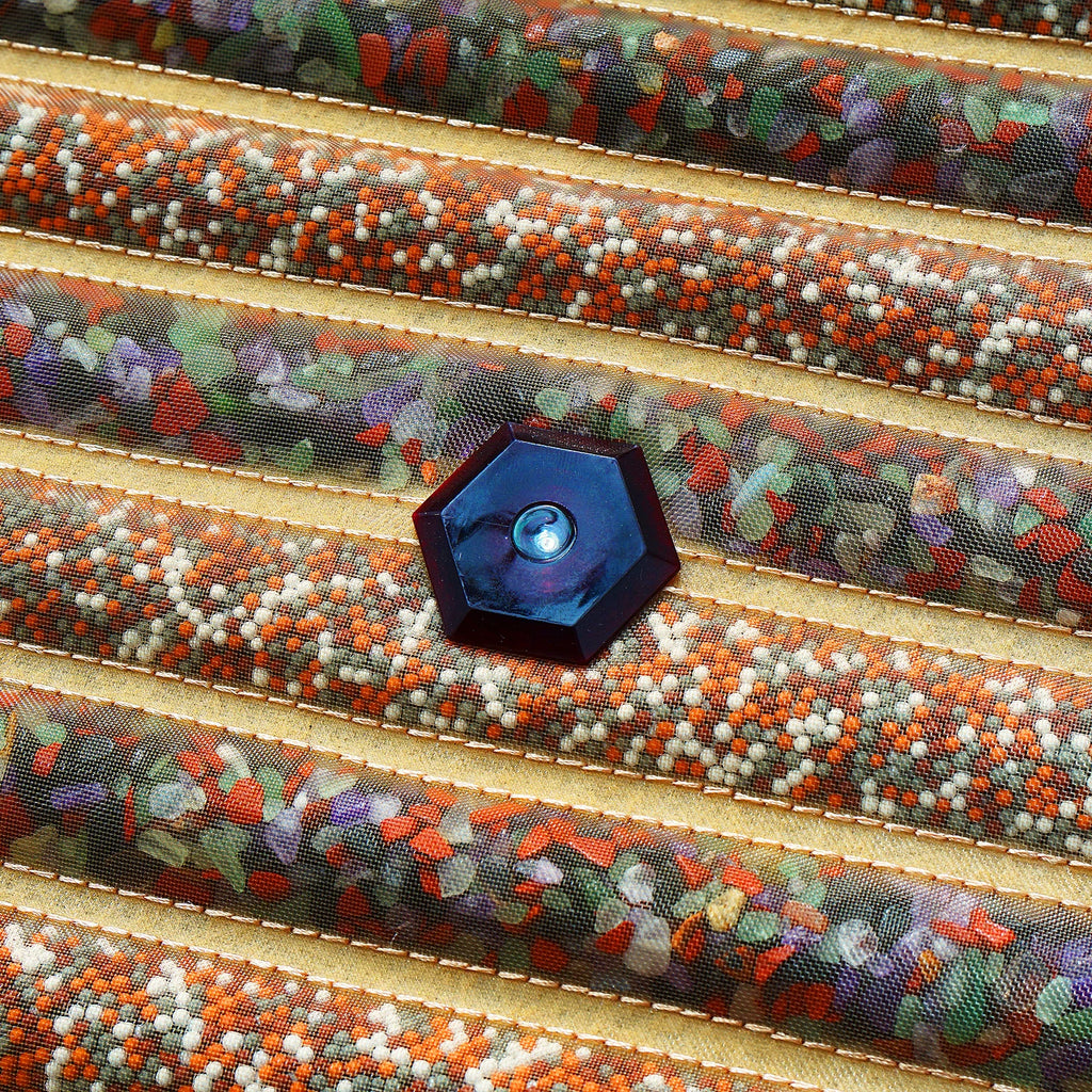 Hexagonal dark purple fidget spinner center cap on a textured sensory mat with rows of multi-colored mineral beads.
