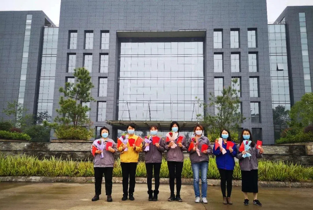 Group of staff wearing masks holding signs in front of a large building entrance
