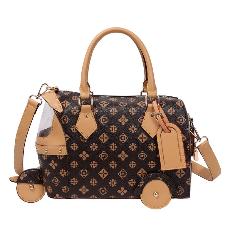 Brown PU leather trunk shoulder bag with tan trim, floral pattern, and playful tricycle wheel and luggage tag details.