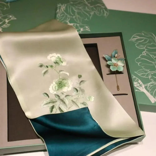 Luxury sage green silk scarf with floral embroidery, teal border, and matching flower brooch in gift box.