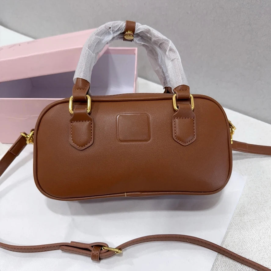 Brown luxury leather trunk handbag with gold hardware, top handles, and adjustable shoulder strap.