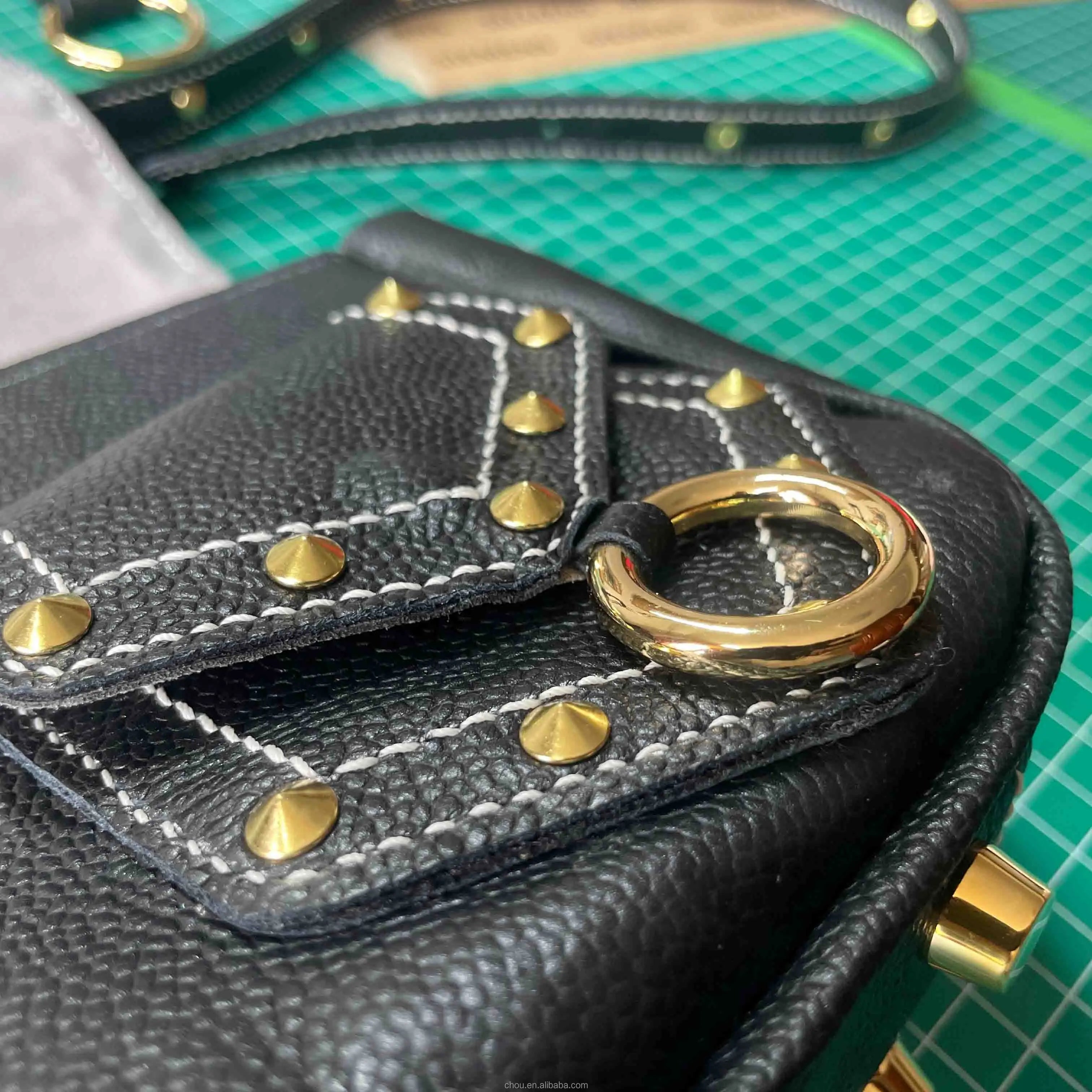 Black pebble-grain calf leather trunk shoulder bag with gold metal studs, white stitching, and a circular ring detail.