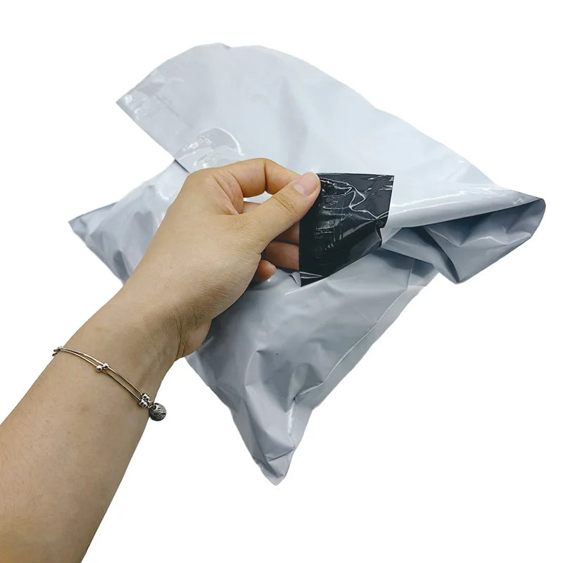 Light gray poly mailer shipping bag with heat-sealed opening, held by hand