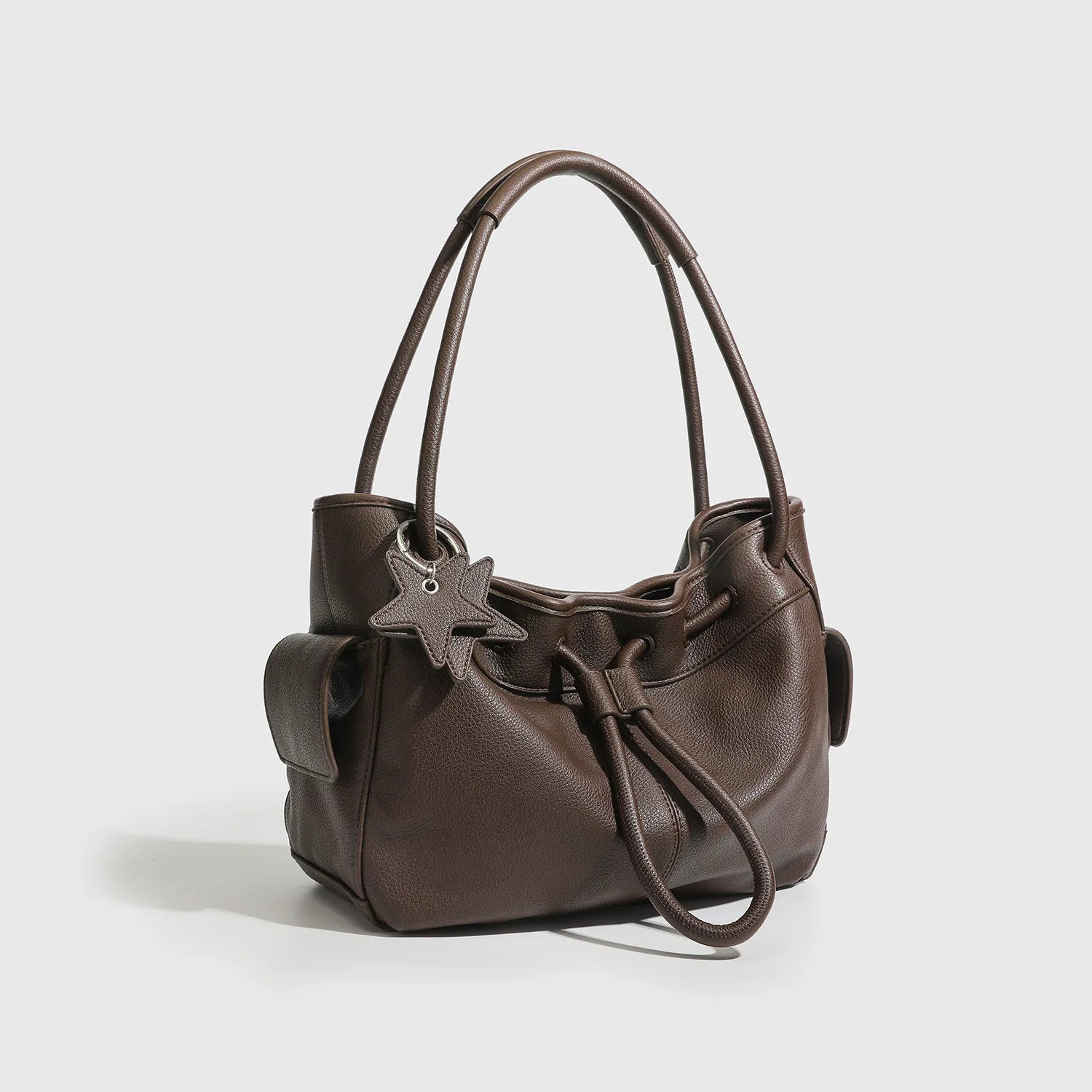 Brown designer underarm shoulder bag with drawstring closure, dual handles, and star charm for daily commuting.