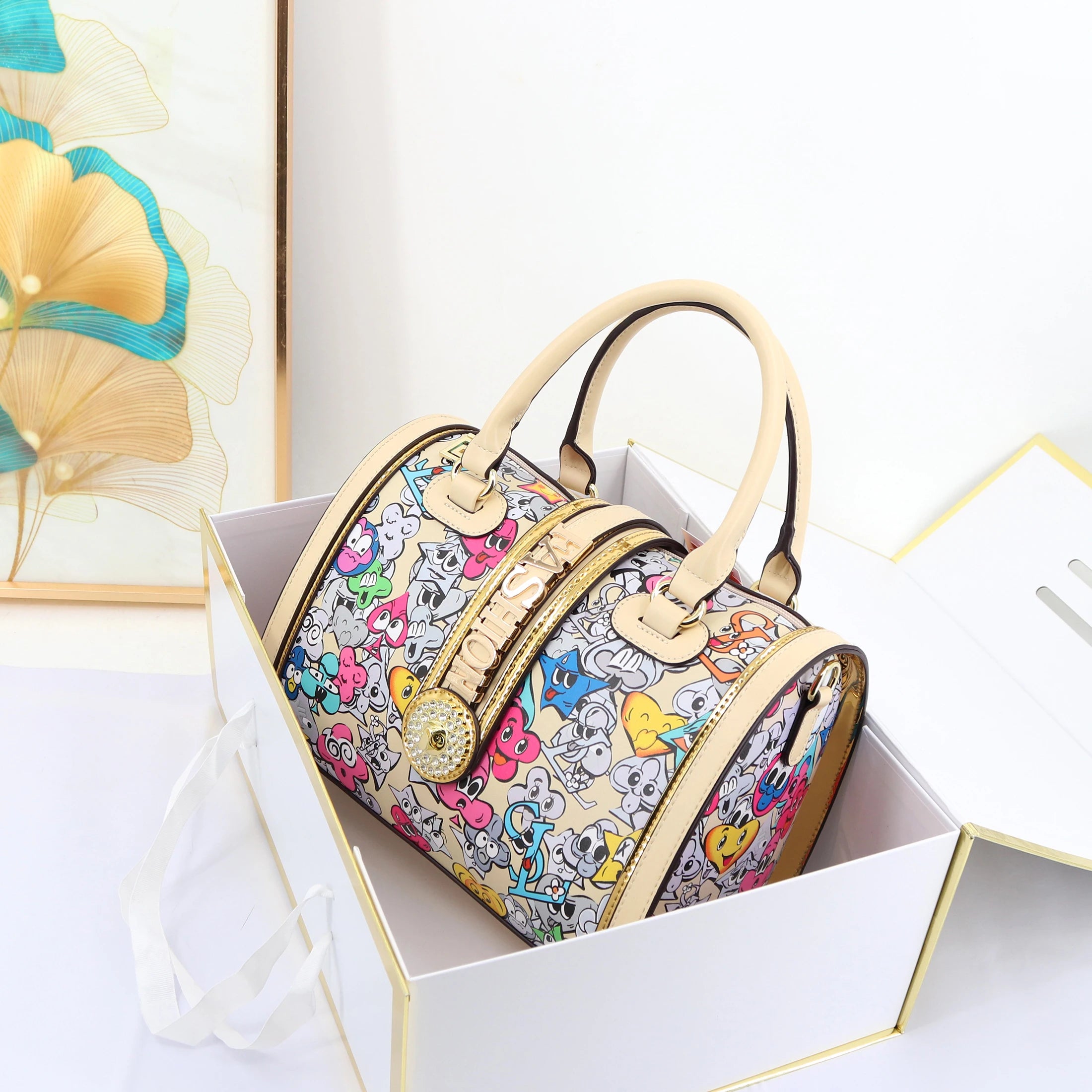 2026 designer trunk handbag with colorful cartoon print, cream leather handles, and crystal-embellished logo center.