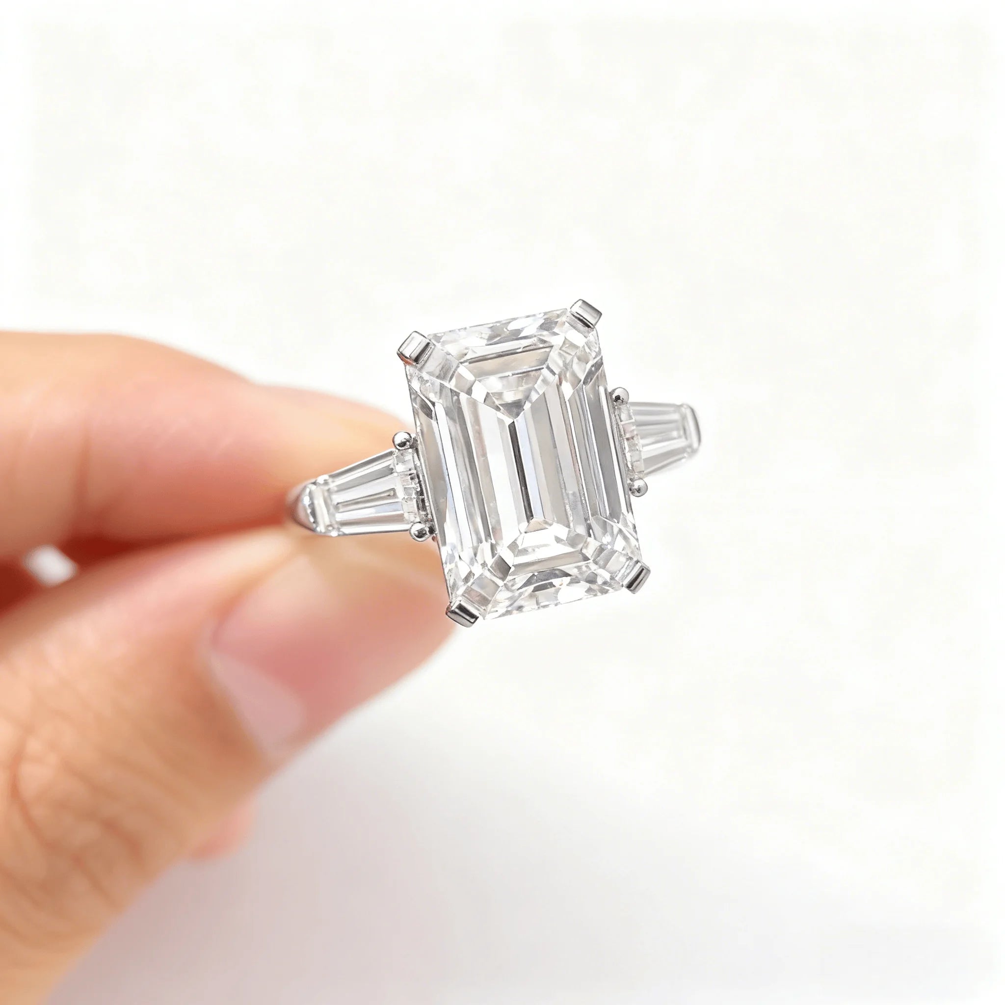 Emerald-cut lab-grown diamond in ring setting, held in fingers for a close-up angle.