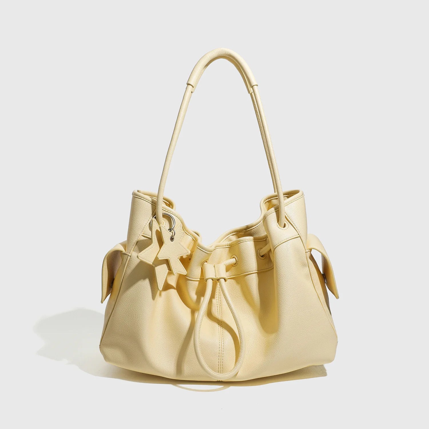 Cream yellow designer shoulder bag, large capacity commute handbag with drawstring closure and star charm accent.