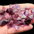 Hand holding purple fluorite crystal rough pieces with faceted angles