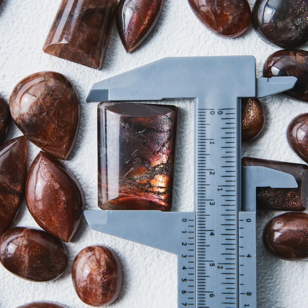 Golden sunstone square pendant stone beside a measuring ruler, glossy copper-brown