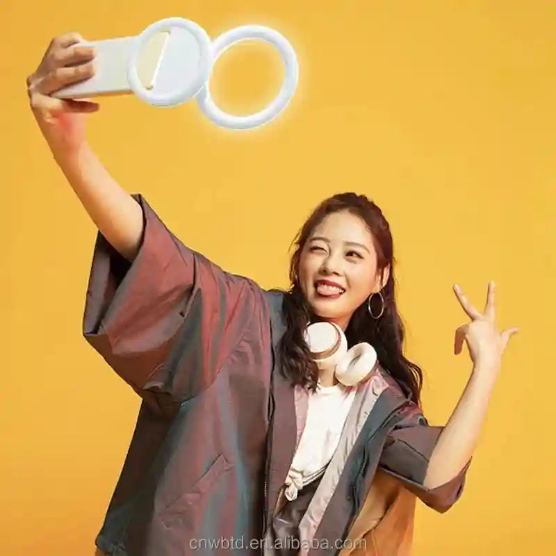 A person holding a small, white, circular handheld ring light for taking selfies against a yellow background.