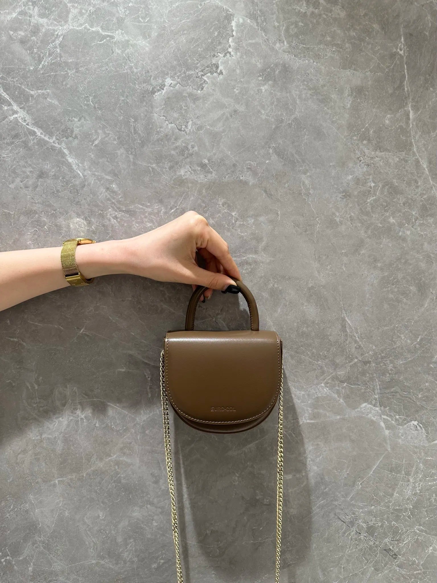 Brown cowhide leather half-moon mini bag with top handle and gold chain strap. Stylish designer evening clutch.