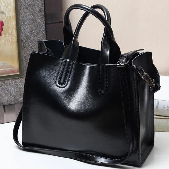 Luxury black genuine leather handbag, classic tote style with top handles and adjustable shoulder strap for women.
