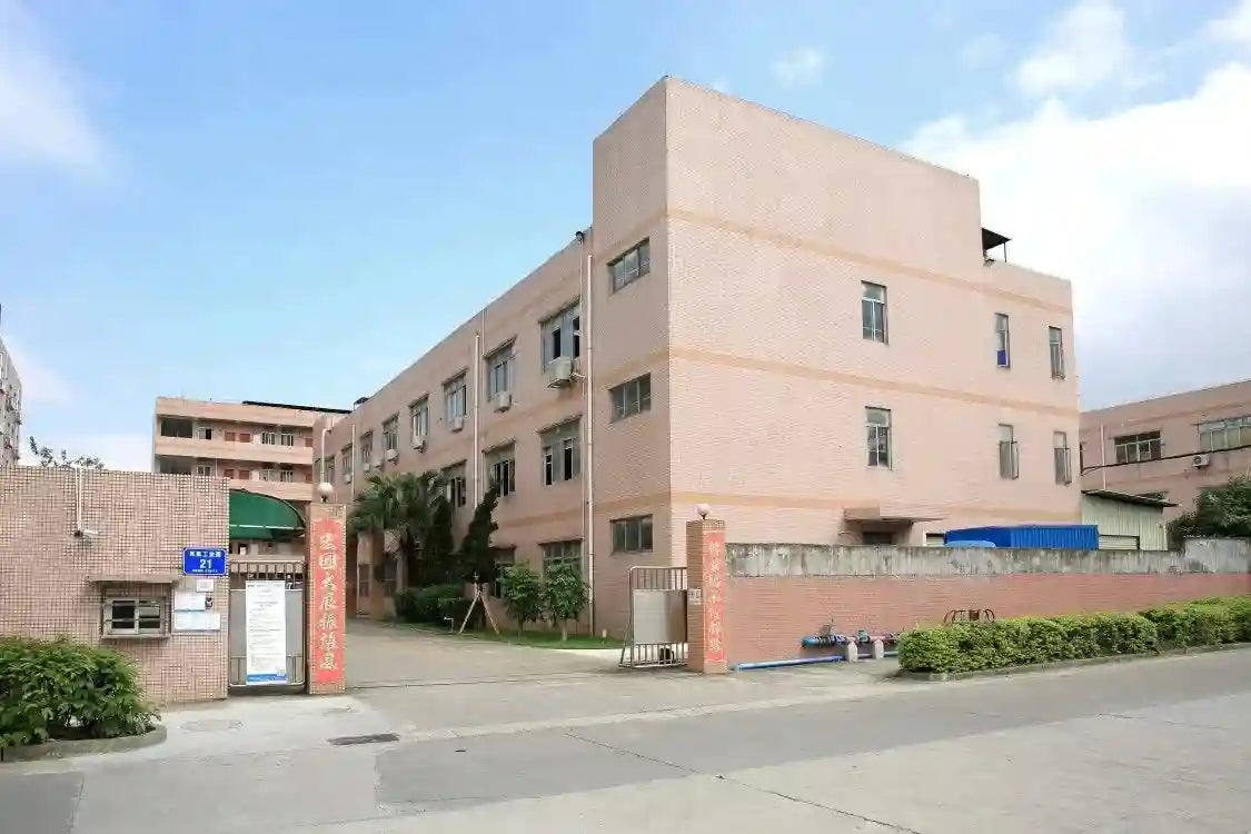 Four-story pink brick factory building with rectangular windows and a gated entrance on a street.