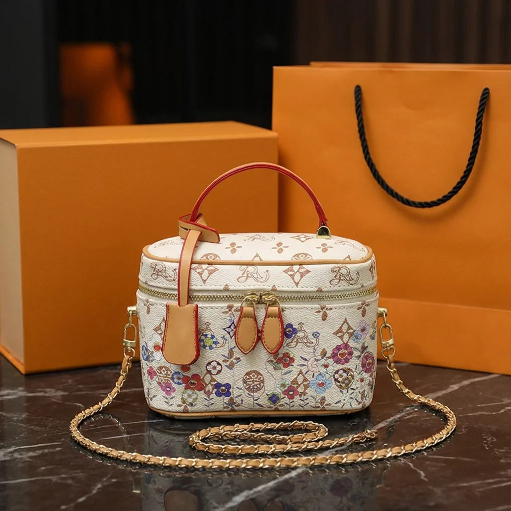White floral print genuine leather trunk crossbody bag with gold chain strap, red handle, and dual zipper closure.