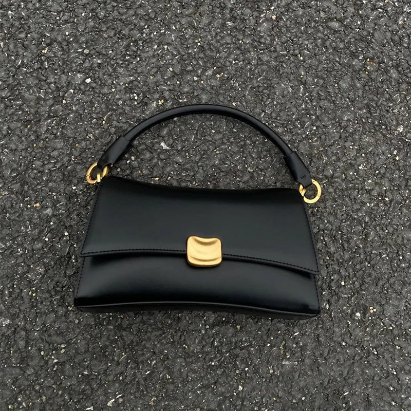 Black designer underarm handbag with gold magnetic clasp, square structure, and dual-ring strap attachment.