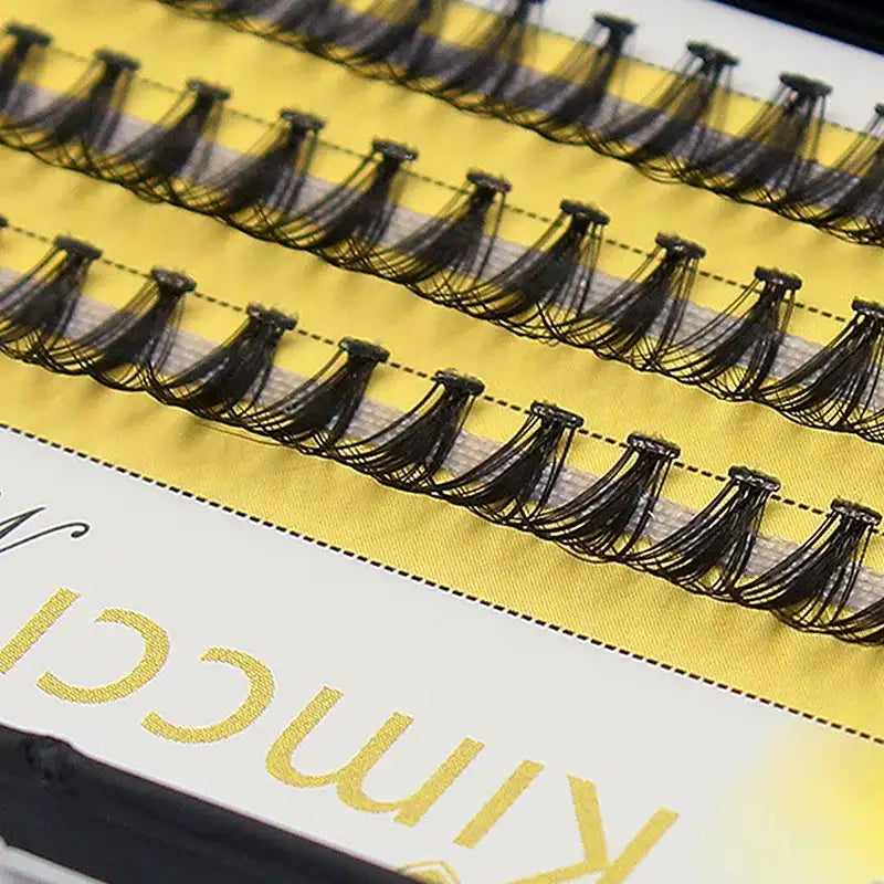 A tray of black 20D Russian volume eyelash clusters arranged in neat rows on a yellow background.