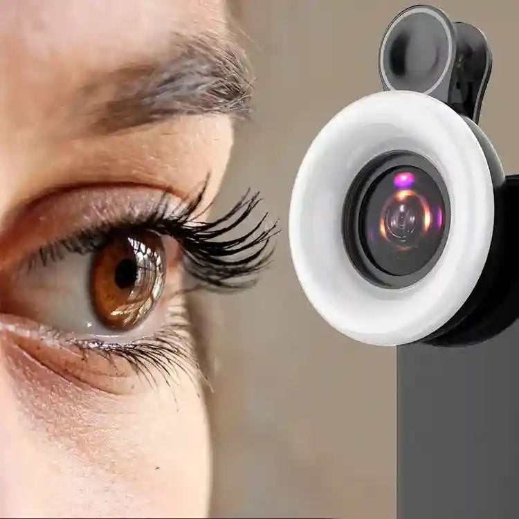 Black clip-on macro lens for smartphones with a circular LED ring light attached, positioned near a human eye.