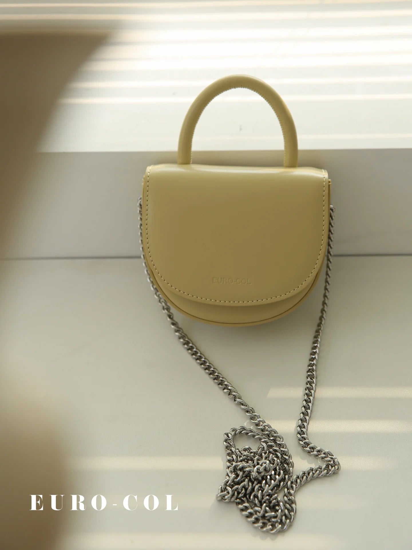 Pale yellow cowhide leather half-moon clutch with top handle and silver chain strap for weddings or evening parties.