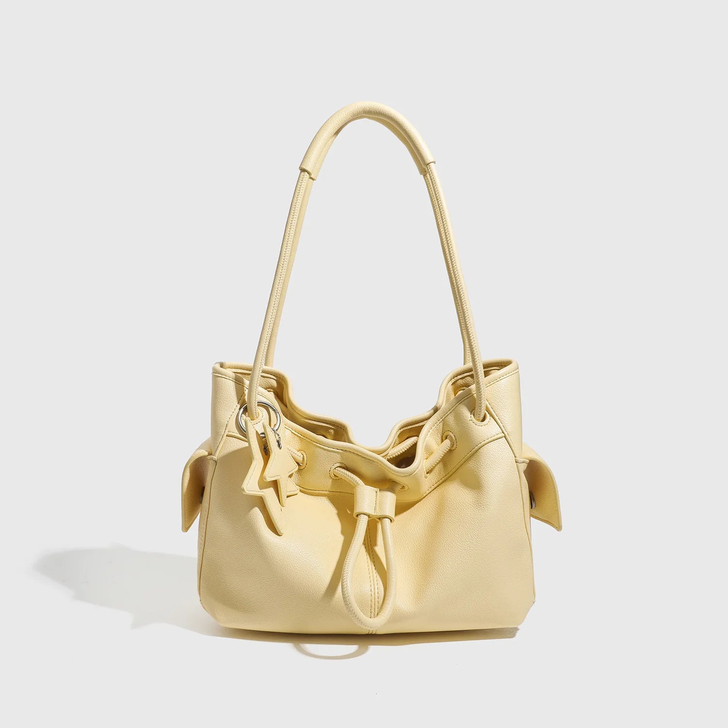 Pale yellow designer shoulder bag with drawstring closure, two handles, and star charm for minimalist commuting style.