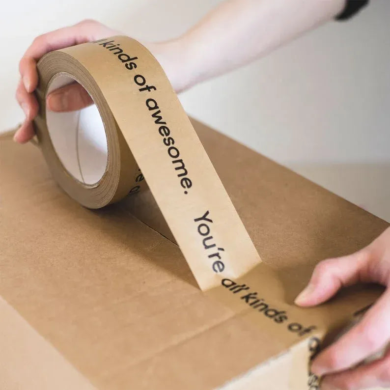 Hands applying brown kraft paper packing tape across a cardboard box seam
