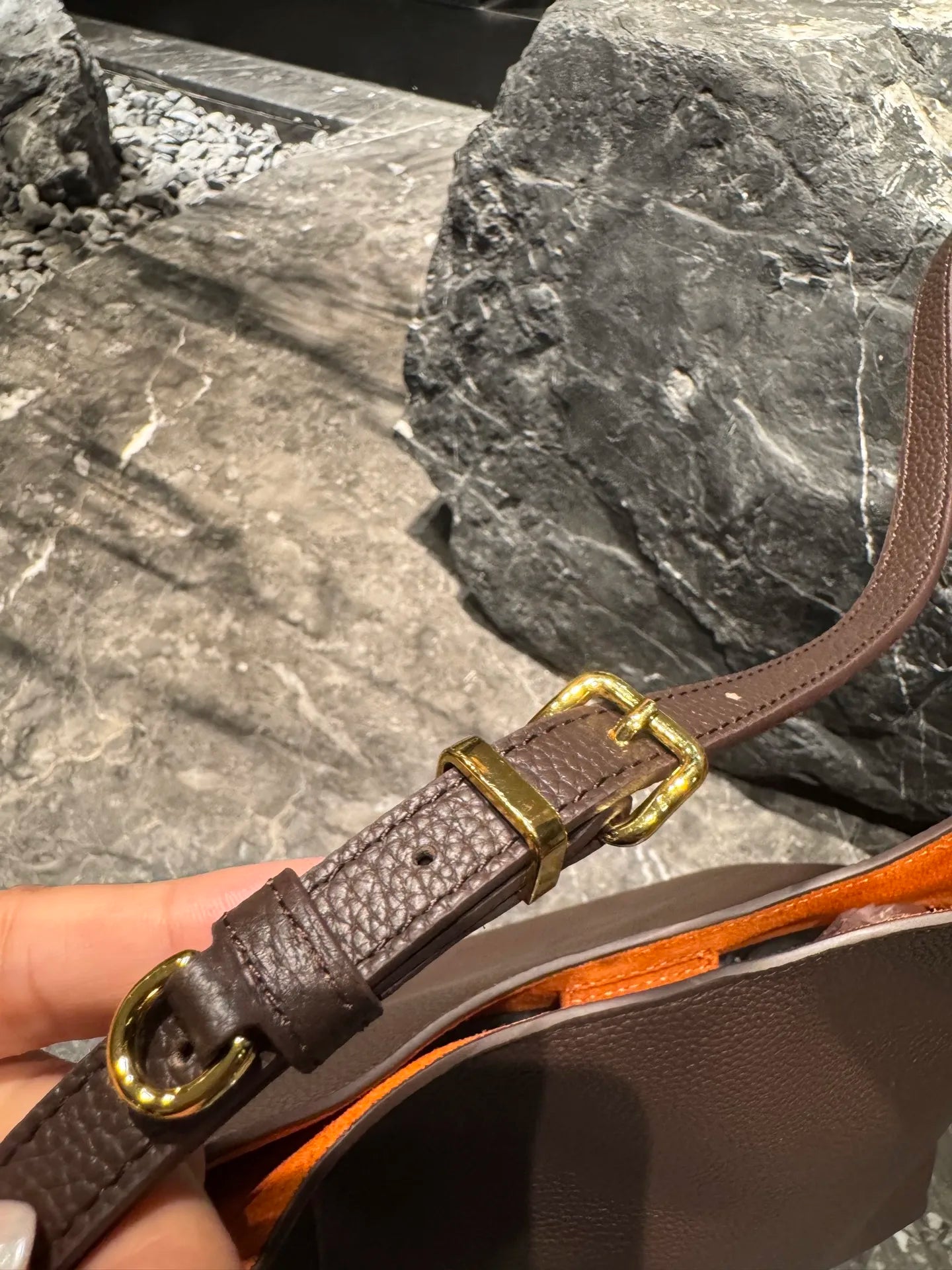 Brown pebble leather hobo shoulder bag with orange interior lining and gold buckle hardware.