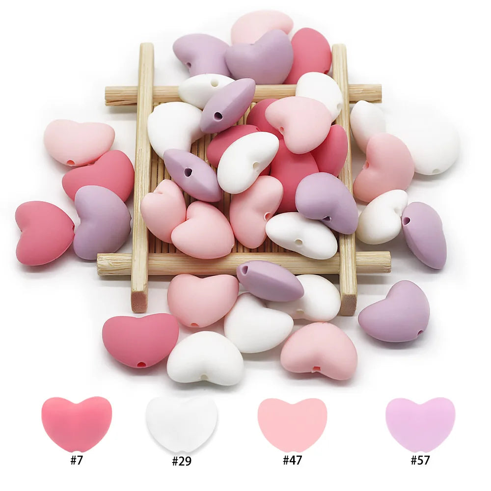 Pink, white, and purple heart-shaped silicone beads for baby teething toys on a wooden rack.