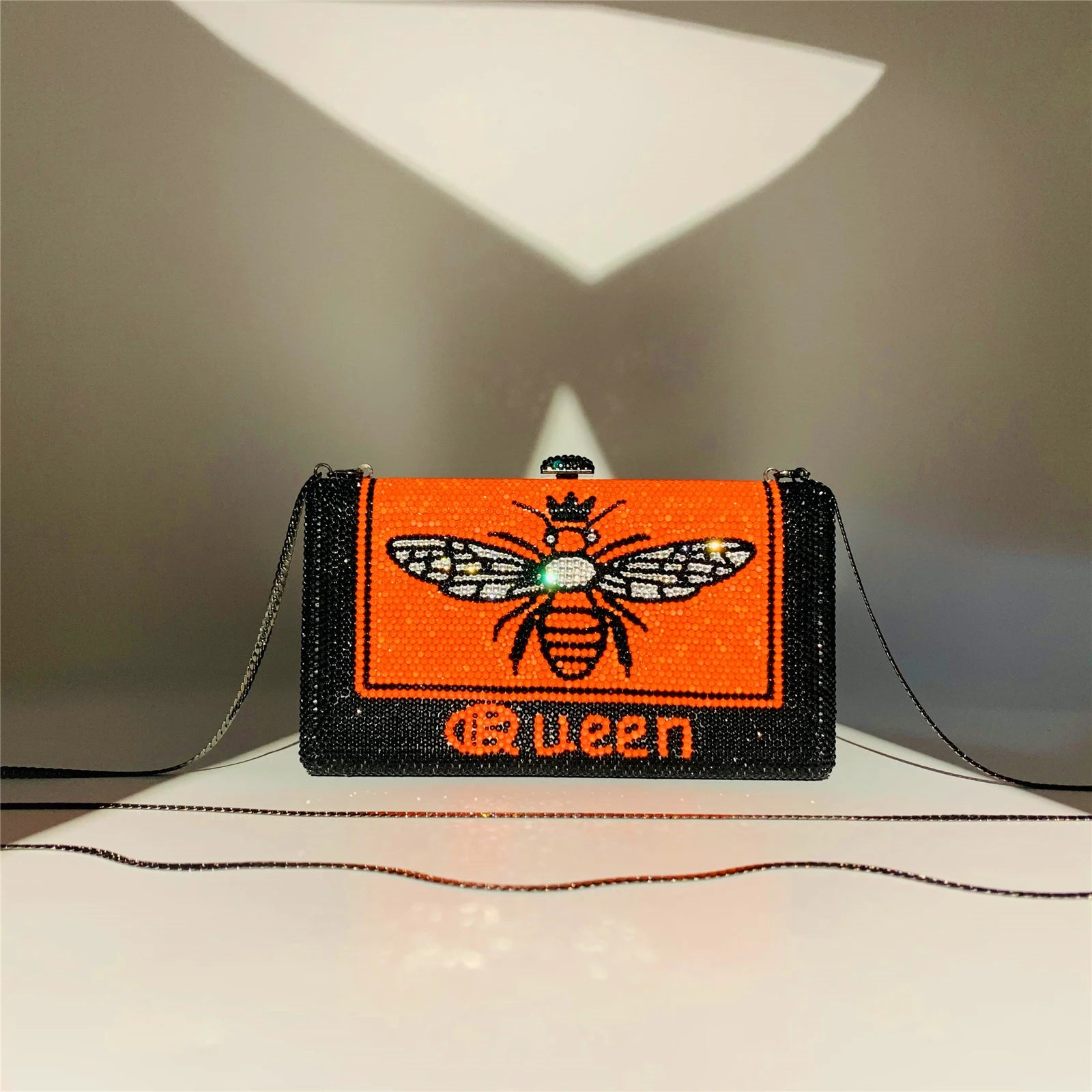 Black and orange rhinestone hard shell evening clutch with bee graphic and "queen" text, includes chain strap.