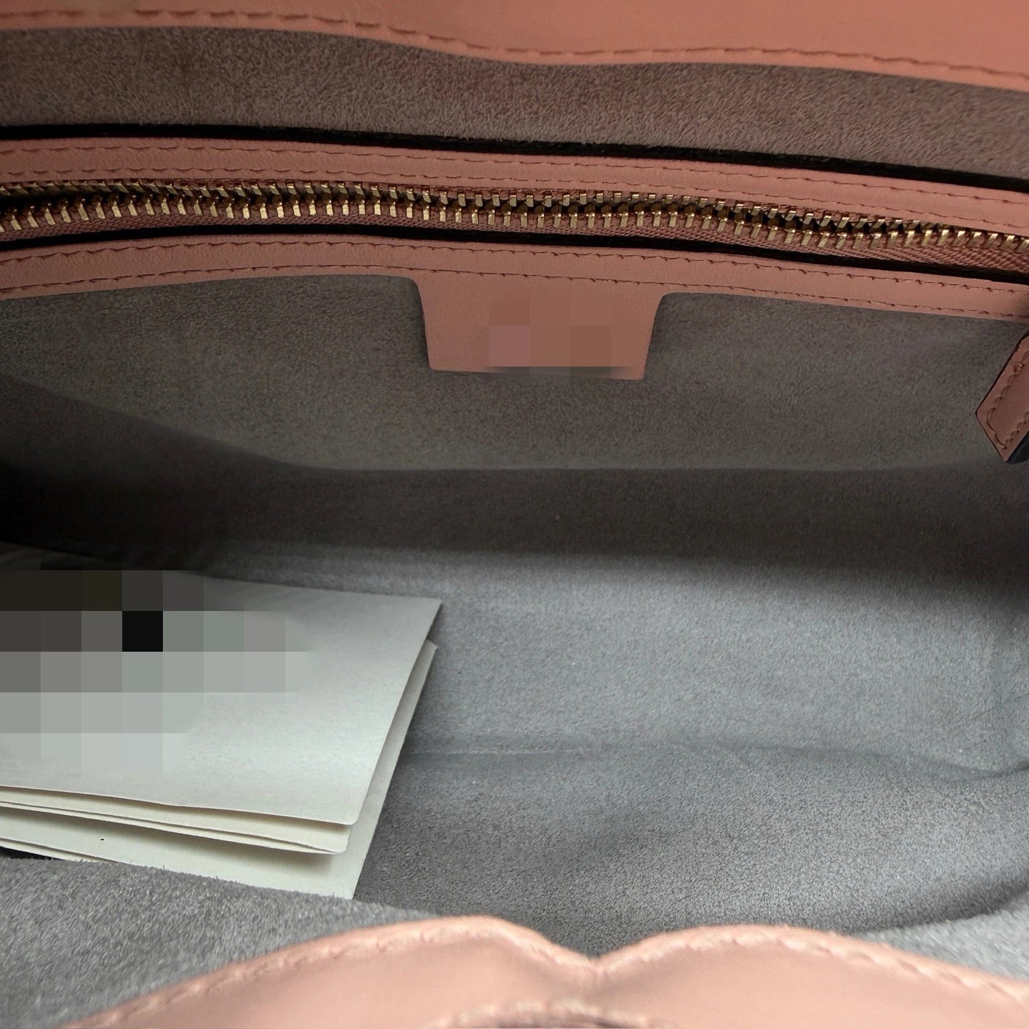 Interior view of a blush pink luxury designer crossbody bag with a spacious grey suede lining and gold zipper.