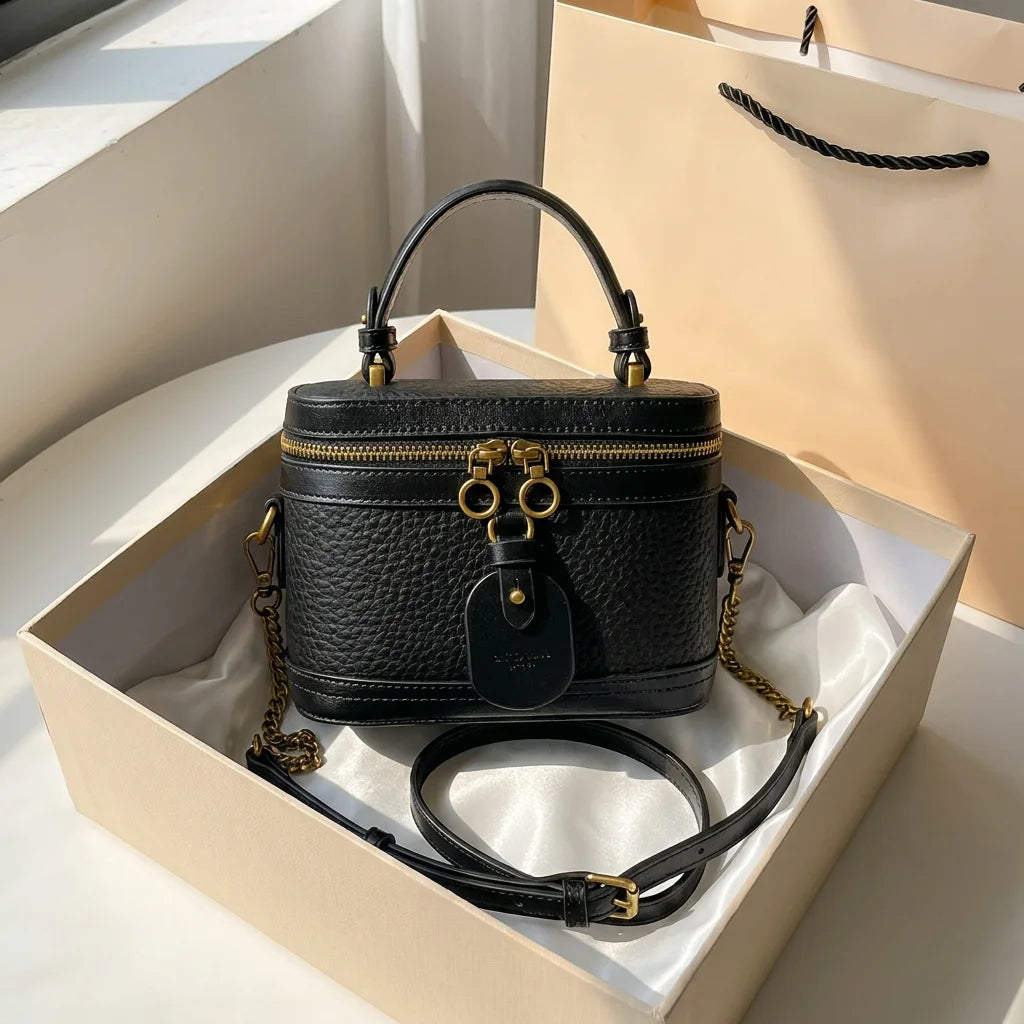 Black caviar cowhide leather vanity trunk bag with gold hardware, top handle, and detachable chain shoulder strap.