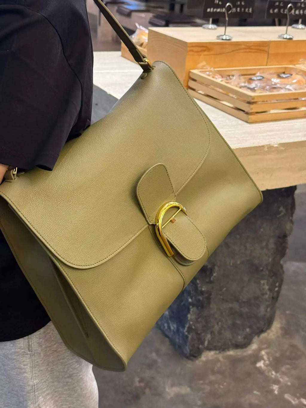 Olive green leather designer shoulder bag with large flap, gold buckle closure, and spacious tote silhouette.