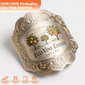 Ornate heart-shaped gold metal bottle label with embossed border and vineyard logo