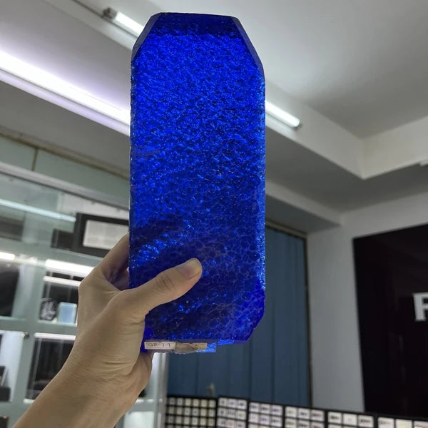 Dark blue synthetic hydrothermal crystal slab with faceted edges, held upright.