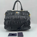 Luxury black pleated leather designer handbag with gold hardware, dual handles, and an optional crossbody strap.