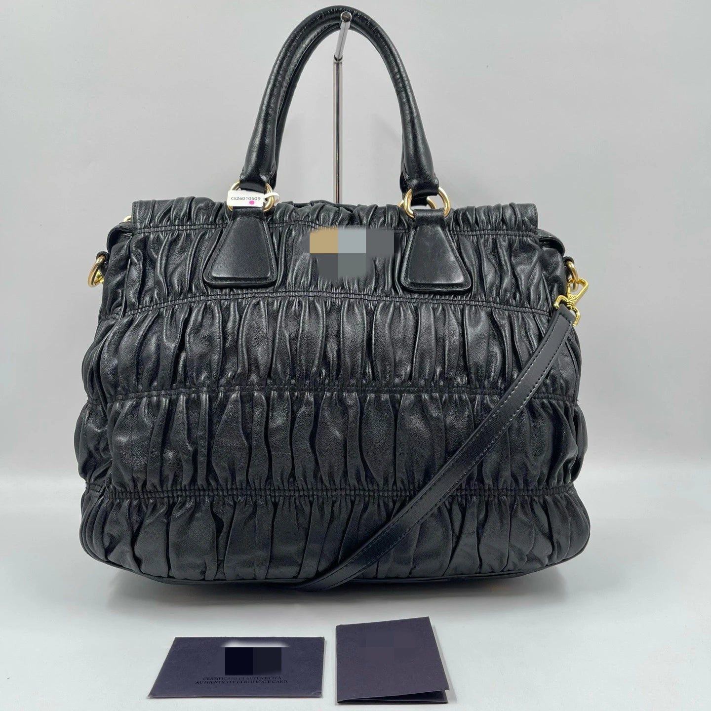 Luxury black pleated leather designer handbag with gold hardware, dual handles, and an optional crossbody strap.