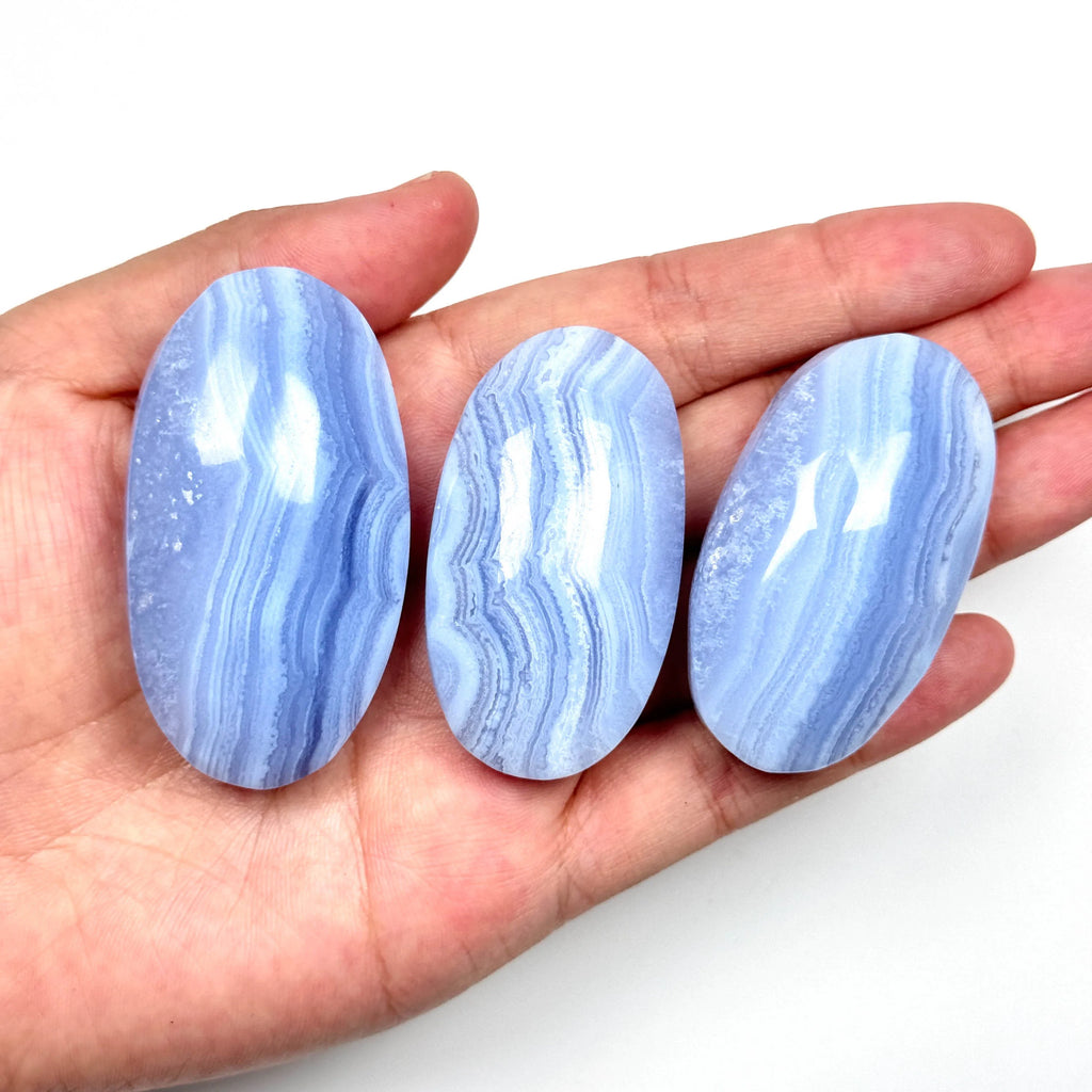 Blue lace agate palm stones held in a hand, smooth oval tumbled stones with striped blue waves