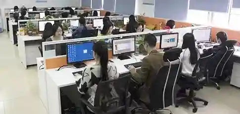 Open-plan office with white workstations, cubicle dividers, and employees working on desktop computers.