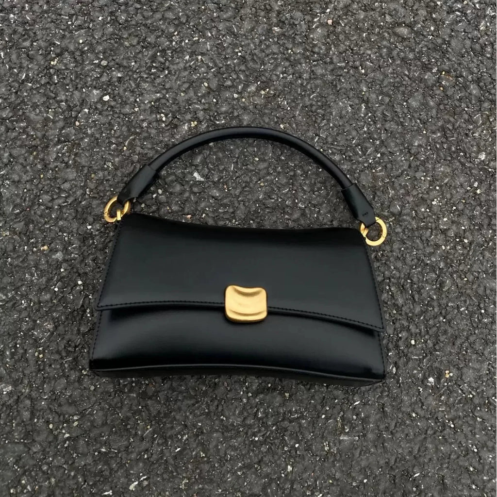 Black designer underarm handbag with gold magnetic clasp, structured square shape, and smooth leather-look finish.