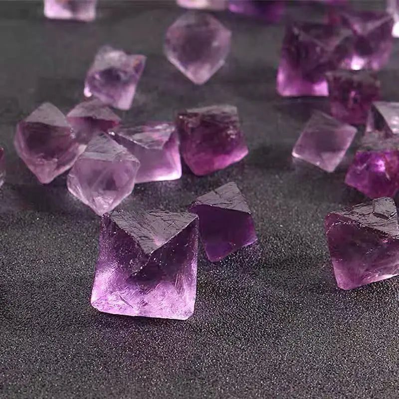 Purple fluorite crystal rough pieces, faceted octahedron shapes on dark surface
