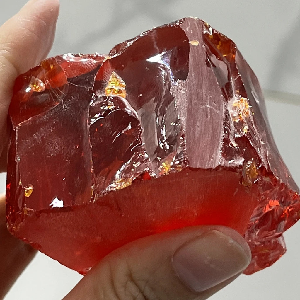 Loose red rough cubic zirconia, uncut faceted chunk with reflective facets, held
