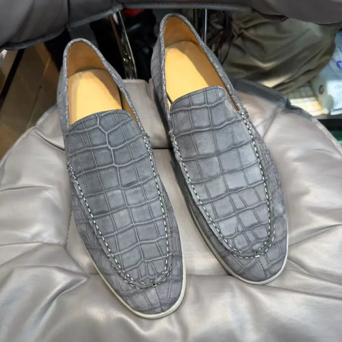 Luxury grey alligator leather loafers with contrast white stitching and minimalist sole, slip-on moccasin style.