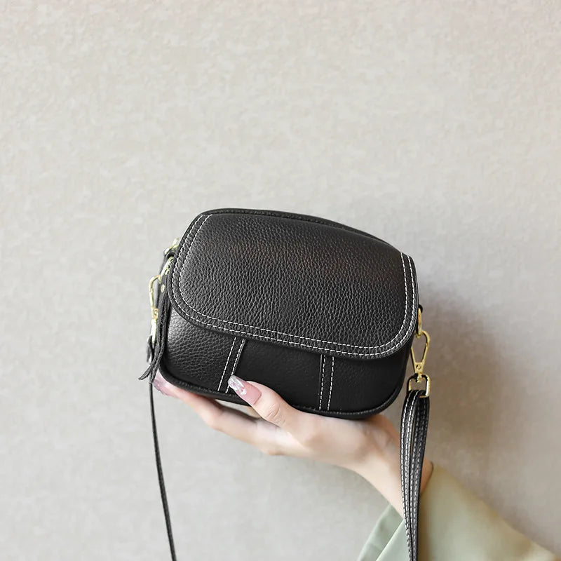 Black mini designer crossbody bag in textured genuine leather with white contrast stitching and gold hardware.