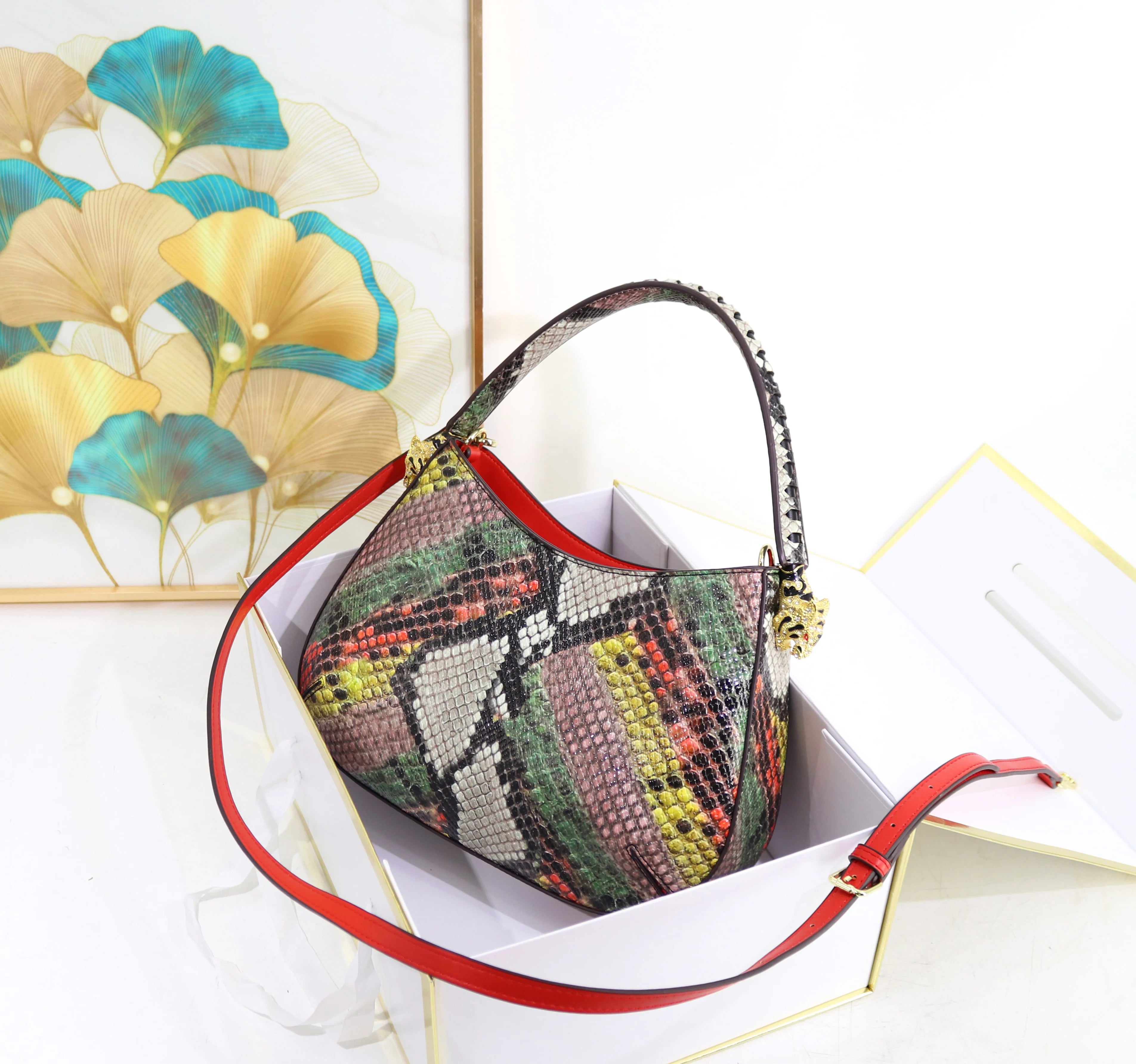 Luxury designer shoulder bag in multicolor snakeskin print with red trim, gold tiger charm, and detachable strap.