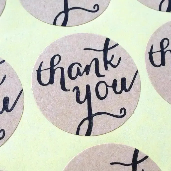 Close-up of round kraft adhesive seal stickers printed “thank you” in black.