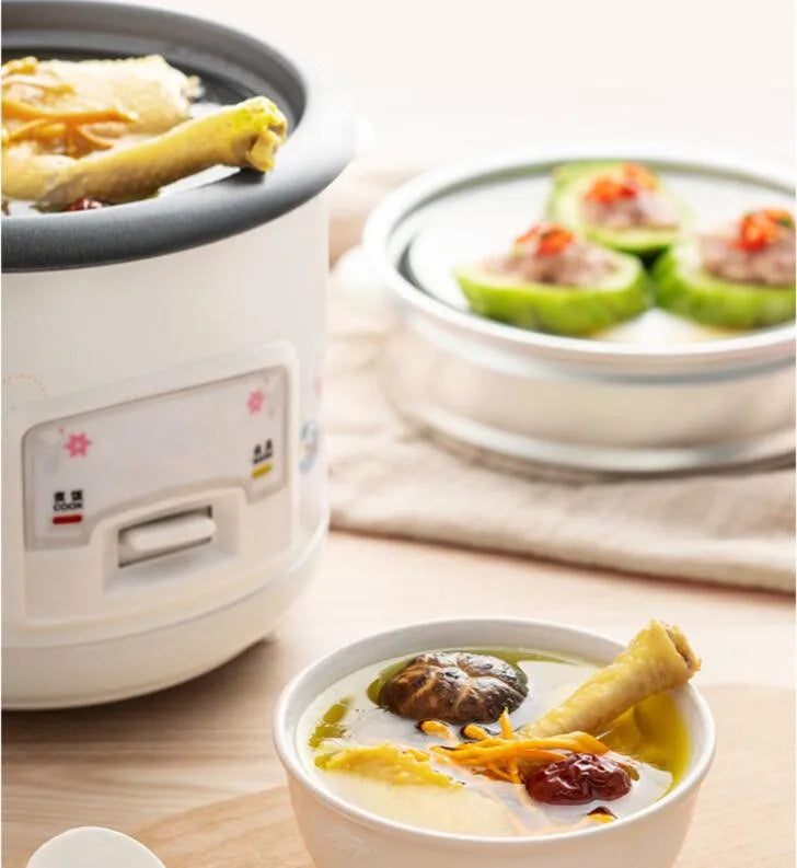 Mini electric rice cooker beside bowls of food, showing outer body and open inner pot