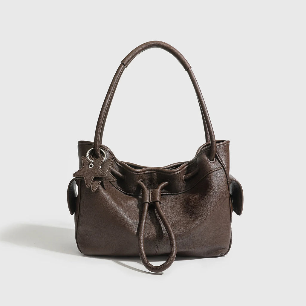 Dark brown pebbled leather shoulder bag with drawstring closure, two straps, and star charm for commuting.